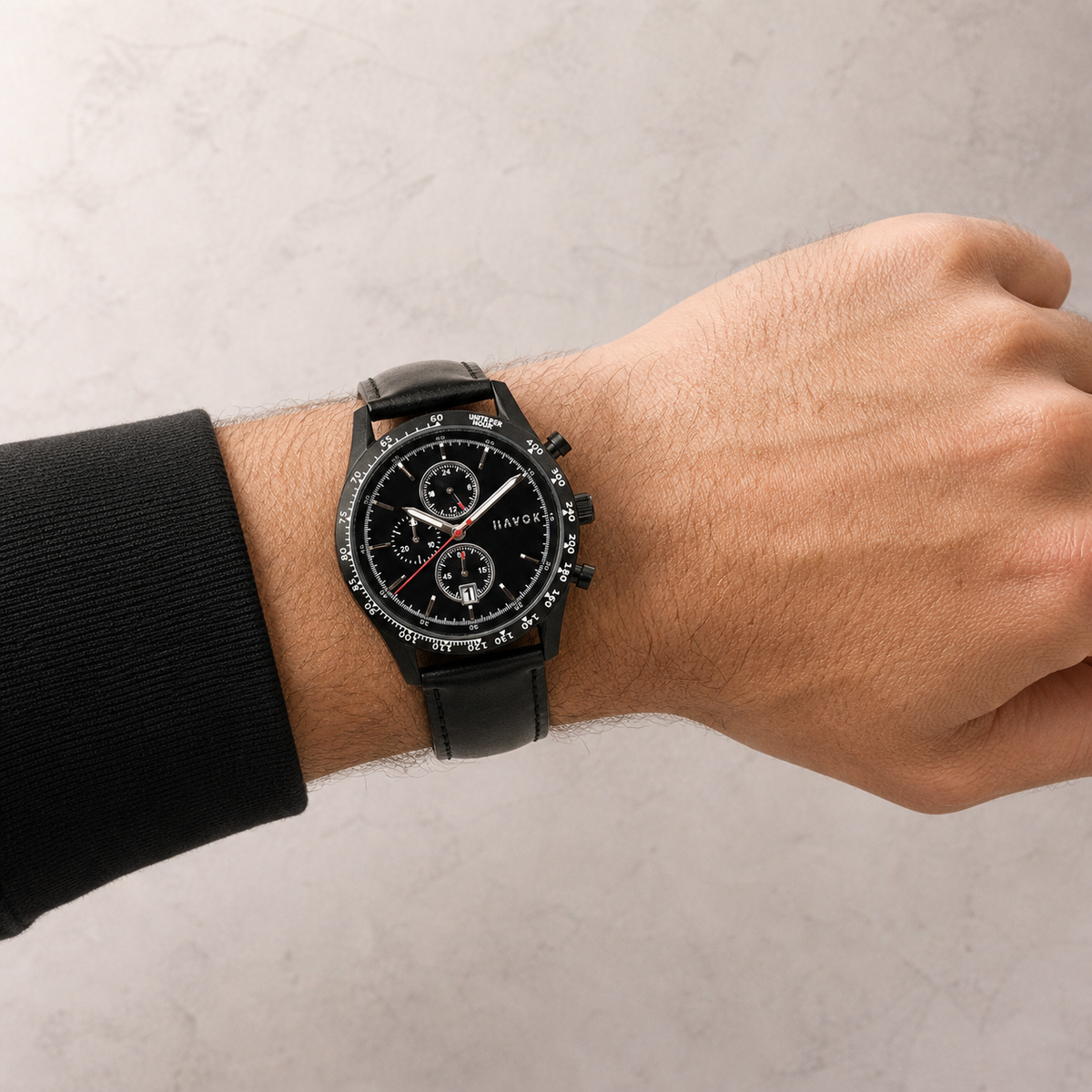 Black wristwatch on a person's wrist against a neutral background