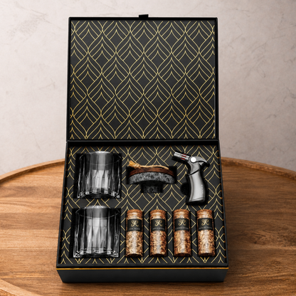 Set of glass tumblers, a brush, and bottles in a decorative box on a wooden surface.