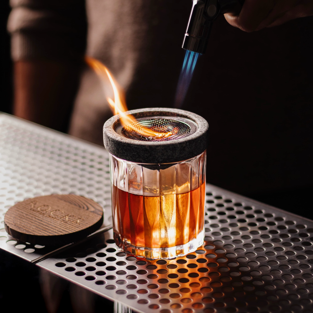 Glass with a metal mesh top being heated by a butane torch on a metallic surface.