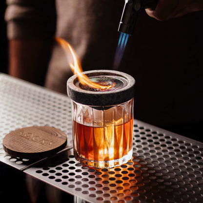 Glass with a metal mesh top being heated by a butane torch on a metallic surface.